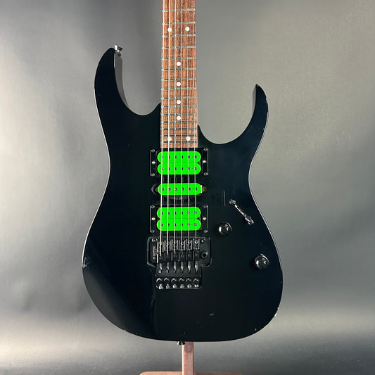Black electric guitar with green pickups on a gray background