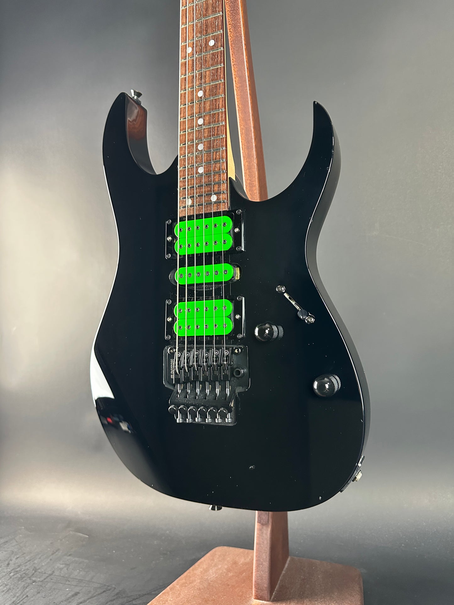 Black electric guitar with green pickups on a gray background