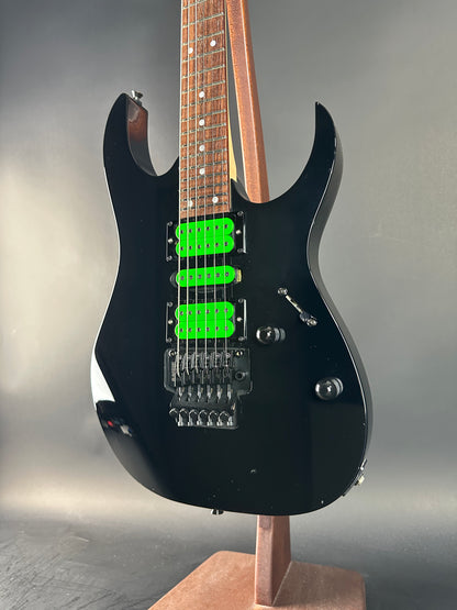 Black electric guitar with green pickups on a gray background