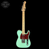 Electric guitar with a turquoise body and red pickguard on a black background, featuring 'Tone Shop' logo.