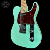 Turquoise electric guitar with a dark brown pickguard on a black background, featuring 'Tone Shop' branding.