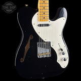 Black electric guitar with a white pickguard on a black background, featuring the Tone Shop logo.