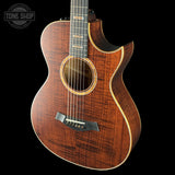 Acoustic guitar with a dark wood finish on a black background, featuring the Tone Shop logo.