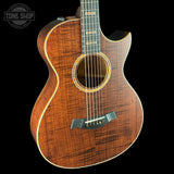 Acoustic guitar with a dark wood finish on a black background, featuring the Tone Shop logo.