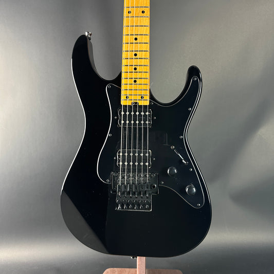 Black electric guitar with a yellow fretboard on a gray background