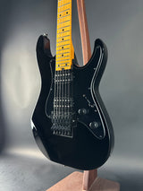 Black electric guitar with a wooden neck on a gray background