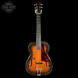 Vintage acoustic guitar with a dark brown finish on a black background, featuring the 'Tone Shop' logo.