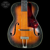 Vintage acoustic guitar with a dark brown finish on a black background, featuring the 'Tone Shop' logo.