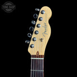 Close-up of a Fender Telecaster electric guitar headstock and upper neck, showing the natural maple wood headstock, six silver tuning pegs, and part of the dark fretboard against a black background.