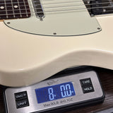 Close-up of a cream-colored electric guitar body resting on a digital scale displaying its weight in pounds and ounces.