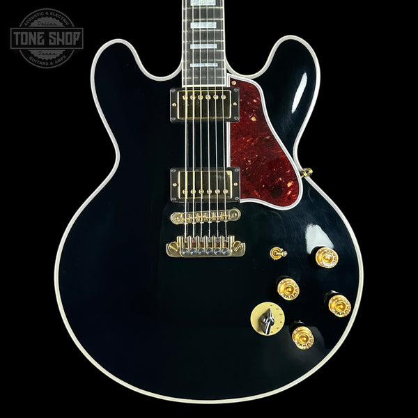 Electric guitar with a black finish and red pickguard on a black background, featuring the Tone Shop logo.