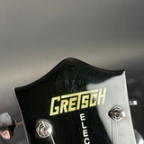 Close-up of a Gretsch Electromatic guitar headstock, showing the gold Gretsch logo and silver tuning pegs on a glossy black finish against a dark gray background.