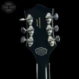 Close-up of the headstock of a black electric guitar against a black background, showing six silver tuning pegs, model text 'ESOMOD04', 'MADE IN INDONESIA', and a 'Gibson' logo badge.