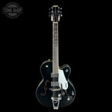A black Gibson electric guitar with a glossy finish, featuring a white pickguard, chrome hardware, and a dark fretboard, shown against a solid black background with a Tone Shop watermark in the top-left corner.