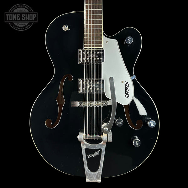 A black Gretsch hollow-body electric guitar with a white pickguard, chrome hardware, and a silver Tremolo tailpiece, shown against a solid black background.