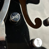 Close-up of a glossy black electric guitar body showing two silver metal tuning pegs with engraved symbols, along with part of a silver headstock and a dark f-hole cutout.