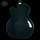 The back of a glossy black double-cutaway electric guitar, shown against a solid black background with a Tone Shop watermark in the upper left corner.