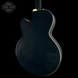 The rear view of a glossy black electric guitar against a solid black background, with a Tone Shop watermark in the upper left corner.