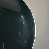 Close-up of a glossy black curved surface with visible scratches and scuffs against a light gray background.