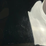 A close-up of a glossy black surface with visible scratches and dust, alongside a large white reflective area on the right.