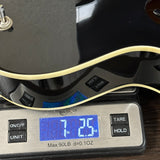 Close-up of a black guitar body resting on a digital kitchen scale displaying 7.25 lbs.