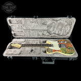 An electric guitar with a colorful floral patterned body and cream pickguard resting inside an open black hard case with gray plush lining, shown against a black background.