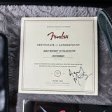 A Fender Certificate of Authenticity card for the Andy Mooney CS Telecaster, displayed on a gray faux fur surface next to a dark leather item.