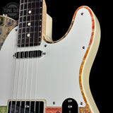 Close-up of a double-cutaway electric guitar body with a white pickguard, black pickups, and a decorative orange-brown wood inlay, shown against a black background.