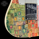 Close-up of an electric guitar body featuring a vintage postage stamp collage design in green, red, blue, and yellow tones, with a black double-cutlass humbucker pickup and chrome hardware.