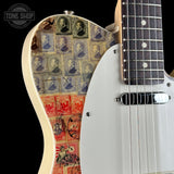 Close-up of an electric guitar body featuring vintage postage stamp artwork in blue, red, and cream tones, alongside a white pickguard and dark fretboard, shown against a black background.