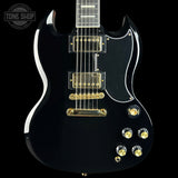 A black electric guitar with gold hardware and white binding, shown from a front three-quarter angle against a black background. A Tone Shop watermark is visible in the top-left corner.