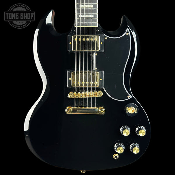 A black electric guitar with gold hardware and white binding, shown from a front three-quarter angle against a black background. A Tone Shop watermark is visible in the top-left corner.