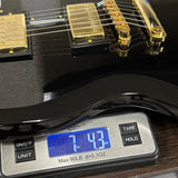 Close-up of a black electric guitar body and pickups resting on a digital scale displaying 7.43 lbs.