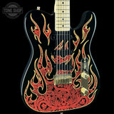 A black electric guitar with a detailed red and gold flame and scroll pattern on the body, shown against a solid black background. A Tone Shop watermark is visible in the top-left corner.