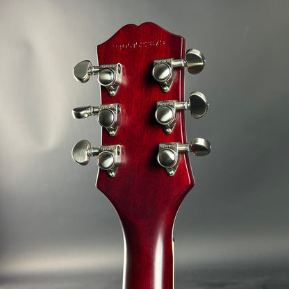 Close-up of a red guitar headstock with tuning pegs on a gray background