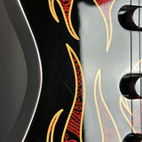 Close-up of a black electric guitar body featuring a flame-style graphic in red and gold with decorative scrollwork.