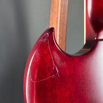 Close-up of a red guitar with a wooden neck on a gray background