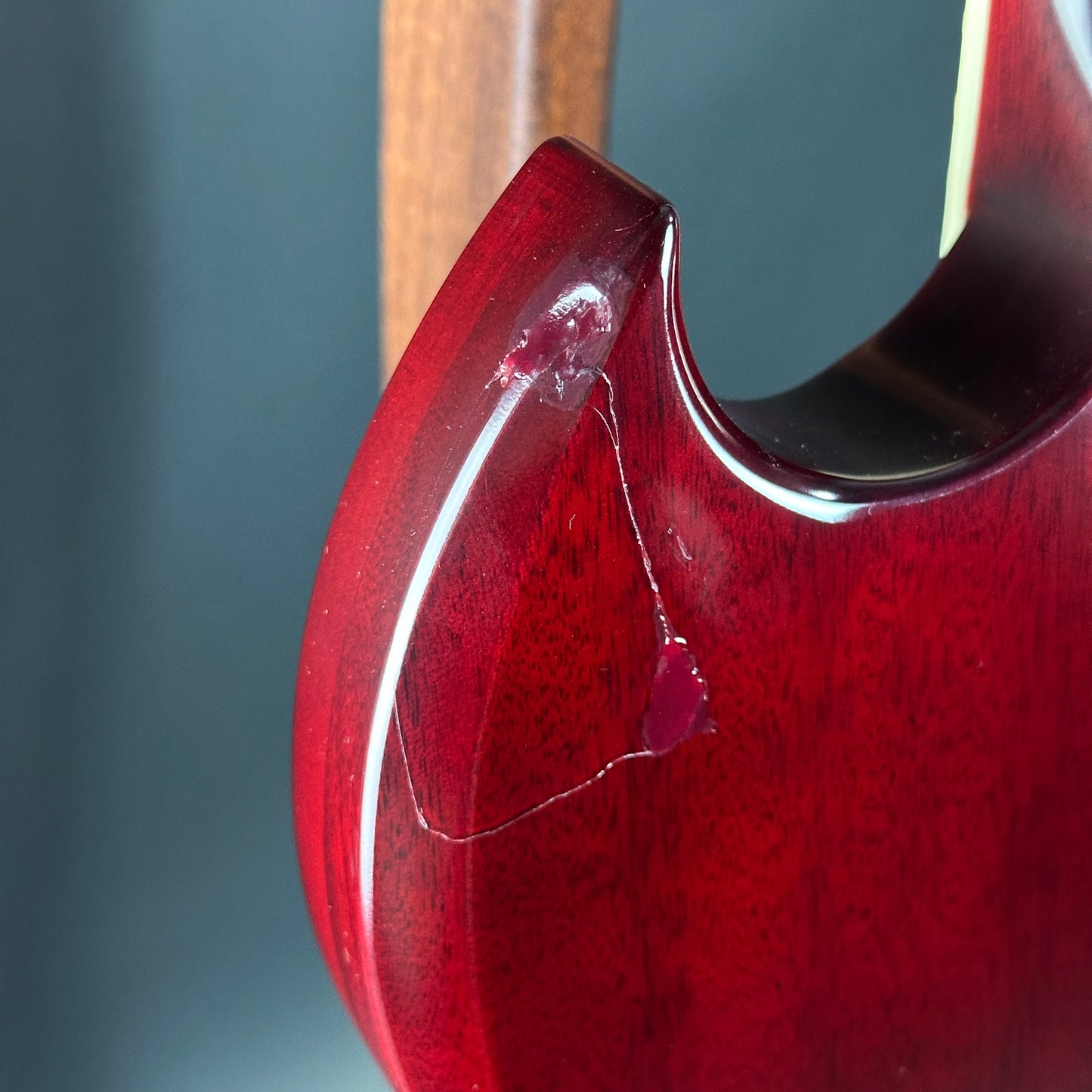 Close-up of a red guitar neck with a wooden fretboard on a gray background