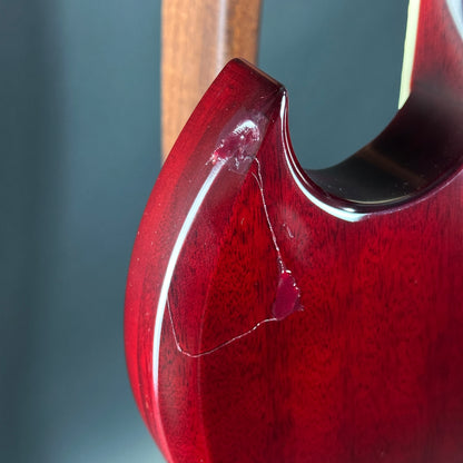 Close-up of a red guitar neck with a wooden fretboard on a gray background