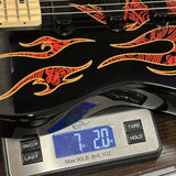 Close-up of a black electric guitar body with red and orange flame-style graphics, resting on a digital scale showing 7.20 lbs.
