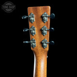 Close-up of the headstock of an acoustic guitar with six metal tuning pegs and a warm brown wood finish, shown against a solid black background. A 'TONE SHOP' watermark is visible in the top left corner.