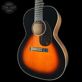 An acoustic guitar with a sunburst finish, featuring a black outer body, warm orange and brown center gradient, and a dark pickguard, shown against a solid black background with a Tone Shop watermark in the top left corner.