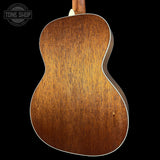 Close-up of the back of an acoustic guitar showing a warm brown wood grain finish and white binding, set against a solid black background with a Tone Shop watermark in the top left.