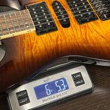 Guitar being weighed on a digital scale with a wooden finish.
