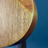 Close-up detail of a wooden curved object, showing the grain and finish against a solid blue background.
