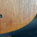Close-up of a curved wooden surface with visible wood grain and a small circular port on the left, against a dark blue background.