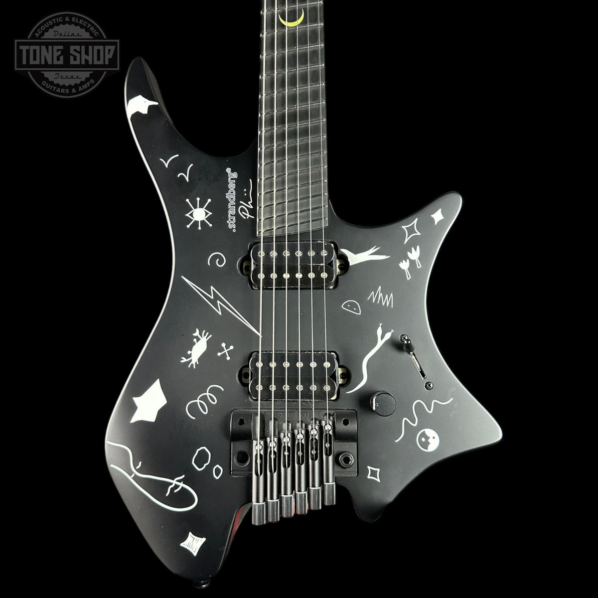 Black electric guitar with white designs on a black background, featuring the 'Tone Shop' logo.