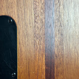Close-up of a wooden surface with visible grain, showing a dark black curved panel secured by two screws on the left side.