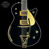 Black electric guitar with gold hardware on a black background, featuring the 'Tone Shop' logo.