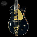 Black electric guitar with gold hardware on a black background, featuring the Tone Shop logo.